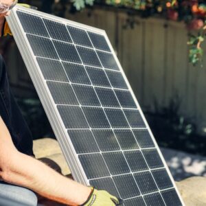 A worker installs a solar panel in a garden, promoting clean energy.